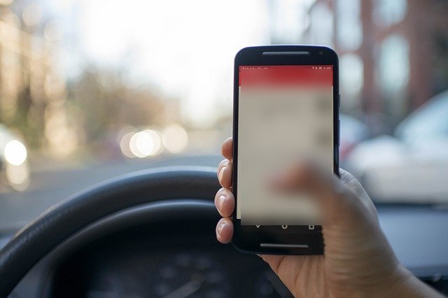 Driver holding a phone in front of the steering wheel, screen blurred.