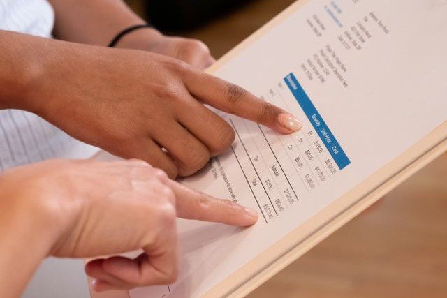 Two people pointing at the line items on an itemized invoice on a clipboard.